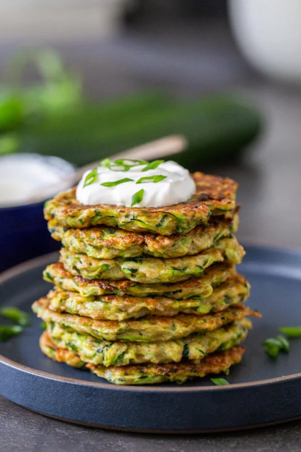 A plate of zucchini fritters stacked up on a gray plate. Photo credit goes to Momsdish Blog