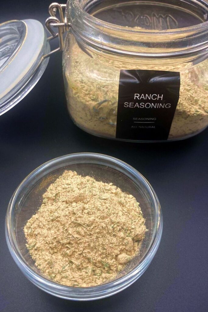 A glass jar with a lid and a small round glass bowl holding Ranch Seasoning Mix.